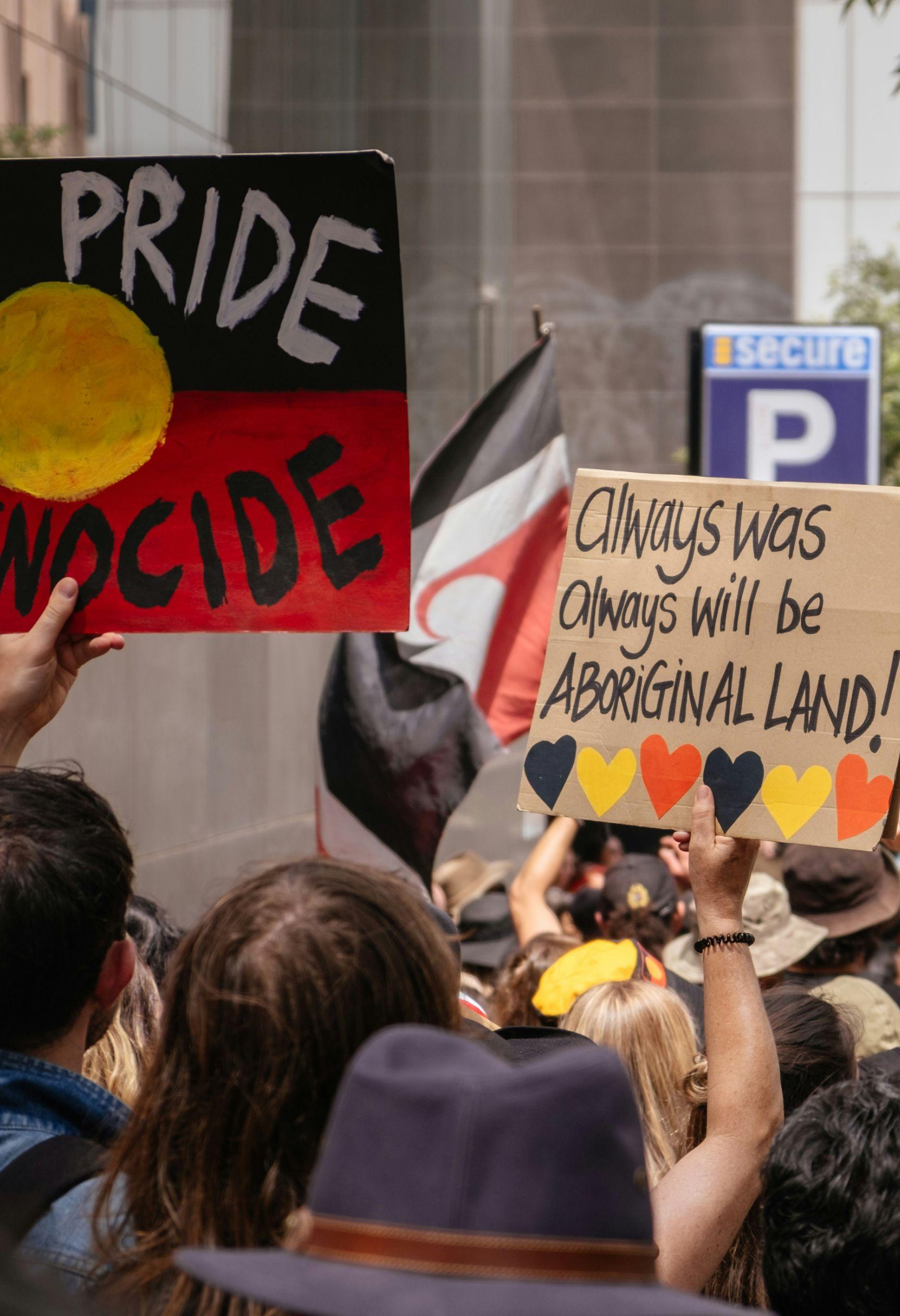 An image from an Invasion Day rally in Melbourne, January 26 2020. People are holding signs reading "Always was, always will be Aboriginal land" and "No pride in genocide".